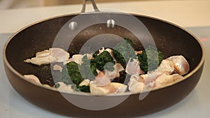 Stewing chicken fillet pieces with spinach on a frying pan