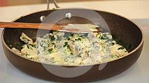 Stewing chicken fillet pieces with spinach on a frying pan