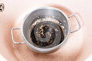 Stewpan with burnt food in pink sink at home