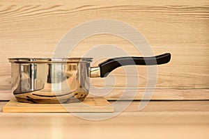 Stewpan on wooden table top. A metal stewpan made of stainless steel against background of beige wooden wall and light table top.