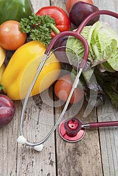 Sthetoscope and fresh colorful vegetables ingredients fo vegan and healthy cooking or salad making on rustic background, top view,