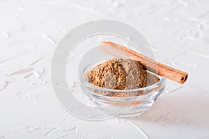A stick of cinnamon lies on a bowl of ground cinnamon