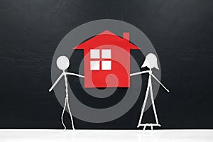 Stick couple figure together holding a red house cutout in black background. Home ownership, housing loan concept.