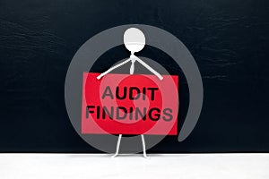 Stick figure holding audit findings placard in black background.