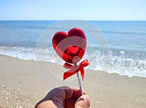 Stick shape volumetric red heart in woman hand against background of blue sea,