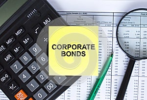 Sticker with text Corporate Bonds lying on the calculator. Magnifying glass with green pen on financial documents