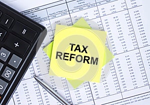 Sticker with text Tax Reform lying on the financial tables. Calculator with metal pen