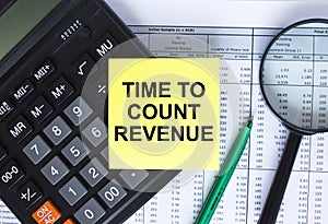 Sticker with text Time To Count Revenue lying on the calculator. Magnifying glass with green pen on financial documents