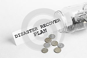Sticking out of a jar of coins a piece of paper with a text DISASTER RECOVER PLAN on a white background