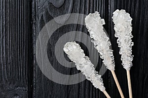 Sticks with sugar crystals on black wooden table, flat lay and space for text. Tasty rock candies