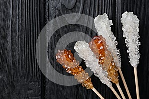 Sticks with sugar crystals on black wooden table, flat lay and space for text. Tasty rock candies