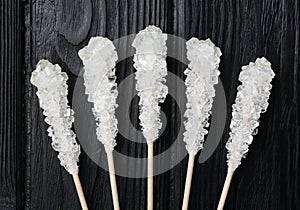 Sticks with sugar crystals on black wooden table, flat lay. Tasty rock candies