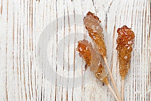 Sticks with sugar crystals on white wooden table, flat lay and space for text. Tasty rock candies