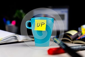 Sticky note on a coffe cup at office desk. Wake up