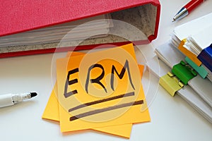 A sticky note ERM Enterprise Risk Management with an abbreviation next to a pile of papers.