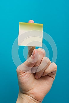 Sticky note, finger up of thumb, yellow reminder on blue background.