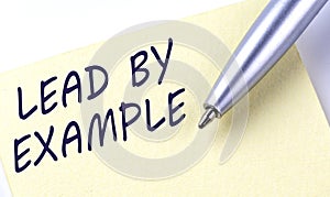 Sticky Note Message LEAD BY EXAMPLE with pen on the white background