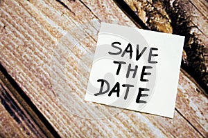 sticky note on the wooden background with the phrase save the date. room for text