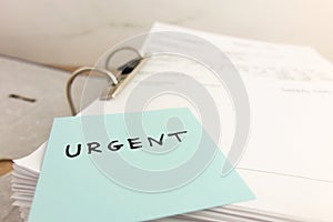 Sticky note with word urgent lying on stack of business paper files