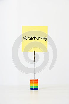 Sticky notepaper with German text Versicherung (Insurance) clipped to a multicolored card holder