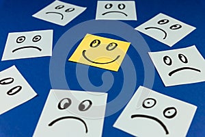 Sticky notes with hand drawn Smiley face and Sad faces on blue background. Positive way of thinking concept