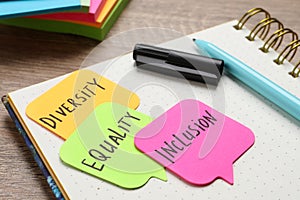 Sticky notes with words Diversity, Equality, Inclusion and stationery on wooden table, closeup