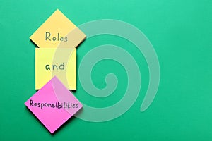 Sticky notes with words forming phrase Roles And Responsibilities on green background, flat lay. Space for text