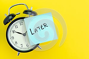 Sticky post with handwriting the word Later stick on alarm clock on solid yellow background with copy space using as