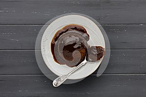 Sticky toffee sponge cake, with a sticky toffee sauce, on a white plate with a spoon, on a dark grey wooden surface with space for