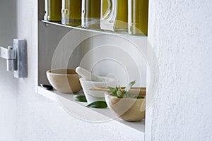 Stii live, bright and sunny detail of shelf in kitchen in house with bottles olive oil wooden bowl mortar green mediterranean