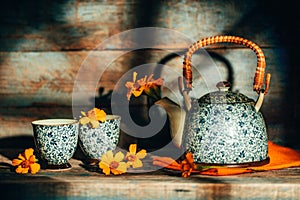 Stiil life with Chernobrivtsi flowers in vintage teapot and cups on rustic old background with sunset light from the