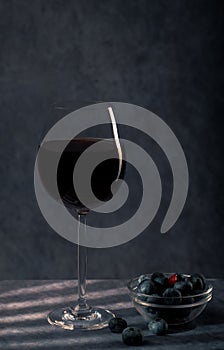 A still-life. A beautiful glass with Red wine and a glass plate with blue berries on a dark blue background with creative Light