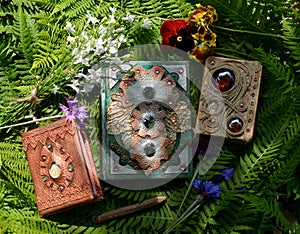 Still life with beautiful magic book of spells or diary with flowers against green leaves. Occult, esoteric and witchcraft concept