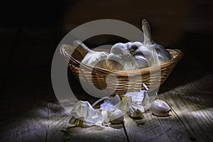Still life on a black background. Garlic in a wicker wooden basket and on a wooden table in the backlight
