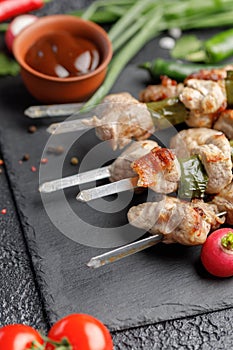 Still life on a black background. Juicy kebabs from pork on skewers. Meat cooked on open fire fresh vegetables and barbecue sauce.