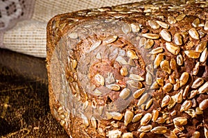 Still life - black bread with sunflower seeds, and a linen napkin on a wooden board, wooden background, hard light