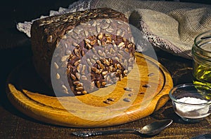 Still life - black bread with sunflower seeds, olive oil and coarse salt in glass jars, a knife, and a linen napkin on a