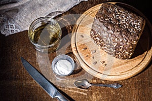 Still life - black bread with sunflower seeds, olive oil and coarse salt in glass jars, a knife, and a linen napkin on a
