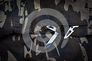 Still life of black and chrome multifunctional pocket tool and small knife on camouflage soldier pant