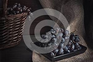 Still life with black grapes and basket on burlap, rustic style, low key