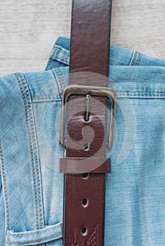 Still life of blue jeans with a brown leather belt on a light wood background