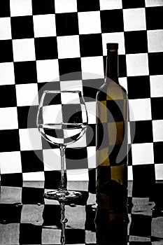 Still life with a bottle and a glass on a background of black and white squares