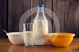 Still life of bottle of milk with glass and two plastic bowls over wooden background