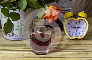 Still life. Bouquet of autumn roses on a wooden table, yellow clock and a glass of homemade wine close-up