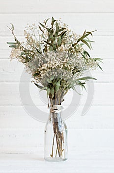 Still life of a bouquet of dried flowers in a glass bottle on a white wooden background. Scandinavian style. Concept of