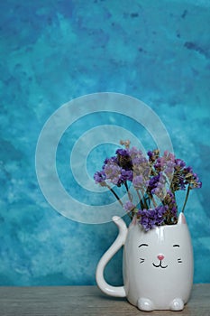 A bouquet of dried flowers in a white cat vase on a blue background