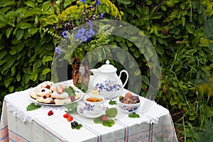 Still life with bouquet of flowers, tea, cookies and berries on table in garden