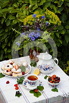 Still life with bouquet of flowers, tea, cookies and berries on table in garden
