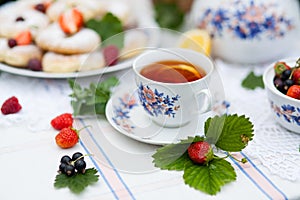 Still life with bouquet of flowers, tea, cookies and berries on table in garden