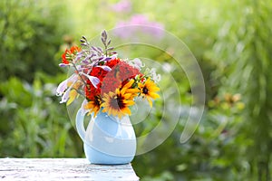 Still life with bouquet of garden flowers in a blue ceramics vase on the table outdoors.